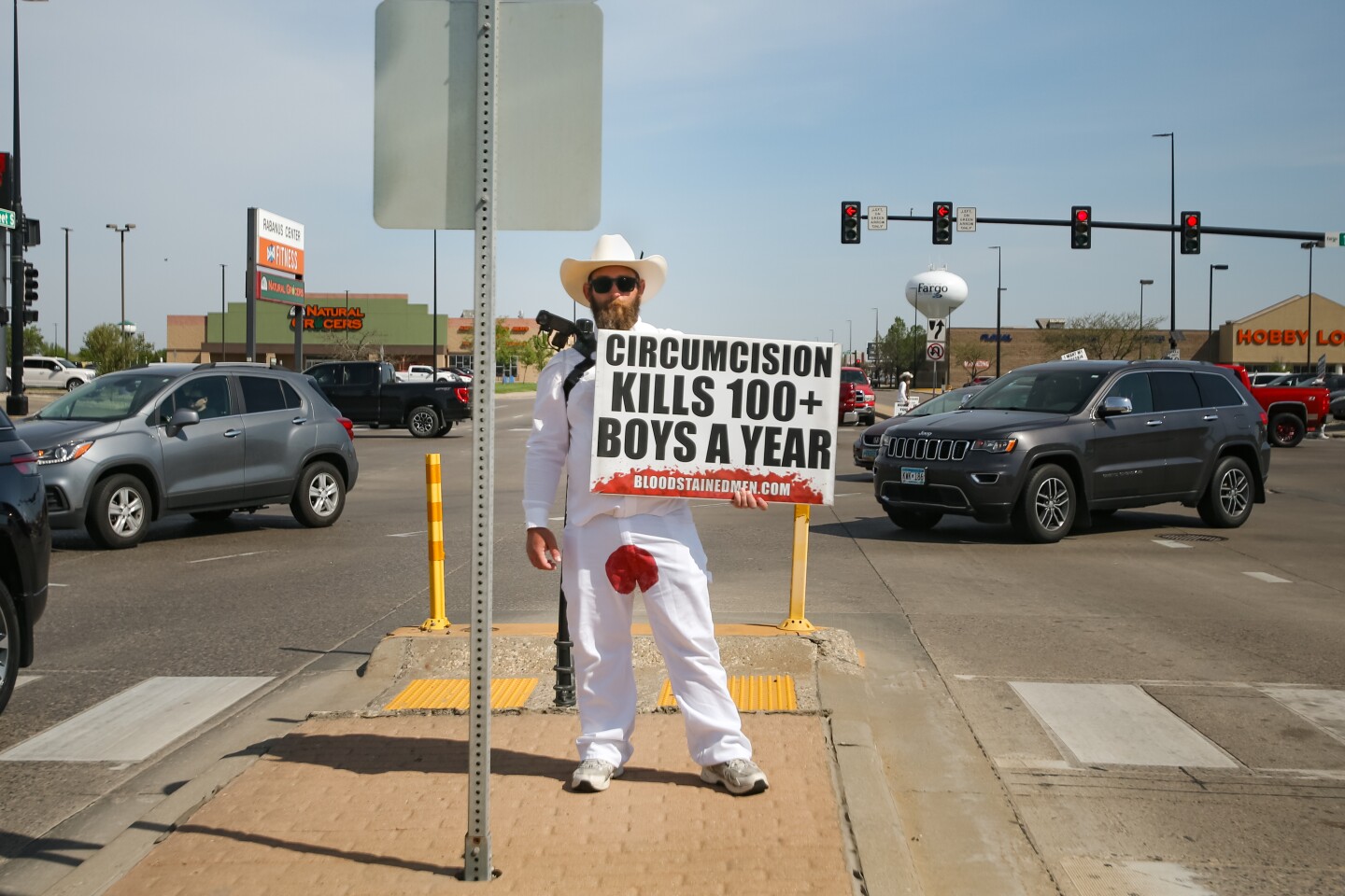 Mathew Kinnison stands at the intersection of 45th Street and 13th Avenue in south Fargo to raise awareness about circumcision with the organization Bloodstained Men on Wednesday, May 14, 2025. Bloodstained Men is an organization that advocates for the rights of children to not be circumcised. Seven men wearing white clothes with a red stain on their pelvic area held signs on each of the corners and the medians at 45th St. and 13th Avenue from 10:30 to noon. They are currently touring the Dakotas and Minnesota.