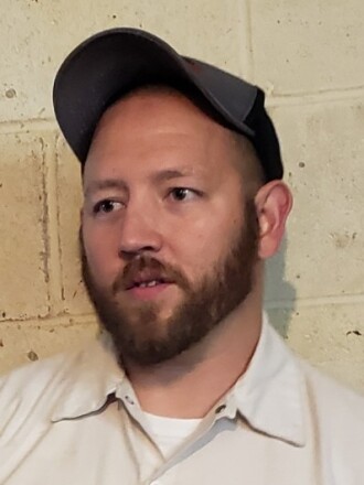 photo of man in tan shirt, wearing a cap