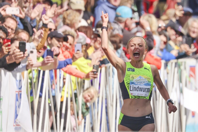 A marathon runner raises in hand in celebration as she crosses a finish line