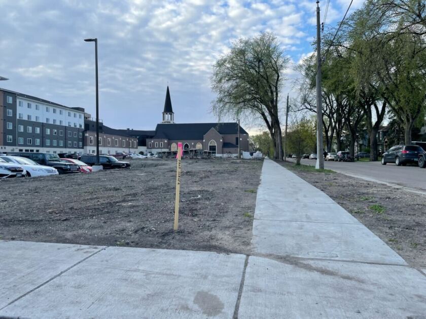 An empty dirt lot with a sidewalk running past it.