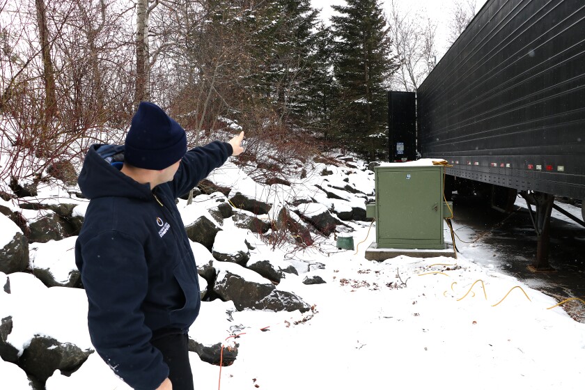 Man points towards camera up near trees.