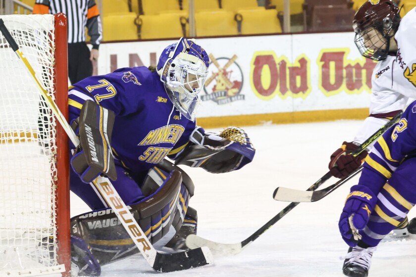 Women hockey players in purple and yellow uniforms compete against players in white and maroon uniforms on an indoor ice sheet.