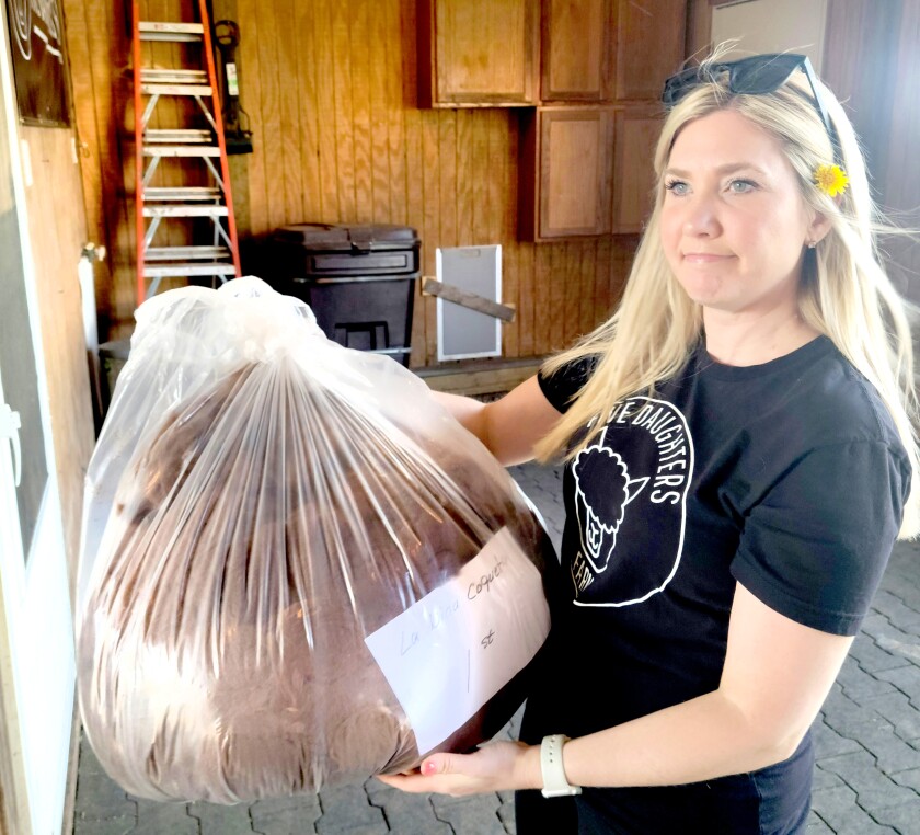 A woman in a black shirt holds a plastic bag filled with brown alpaca fiber.