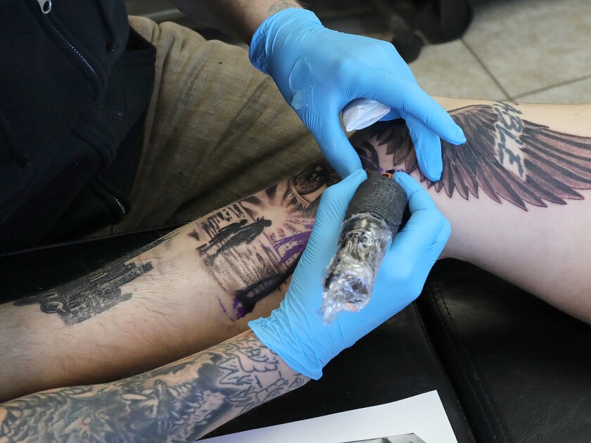 Tattoo artist Dick Davis works on a leg piece for Giovanni Saldavir,