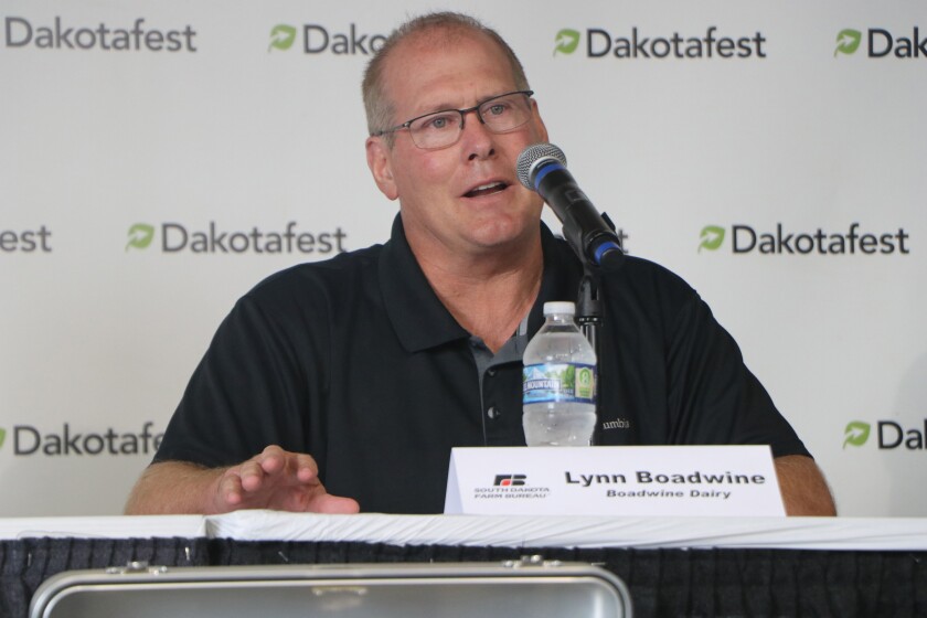 A man in a black shirt sits behind a microphone, describing technology on his dairy farm.