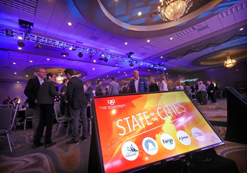 A screen reads State of the Cities in the foreground of a bustling banquet hall.