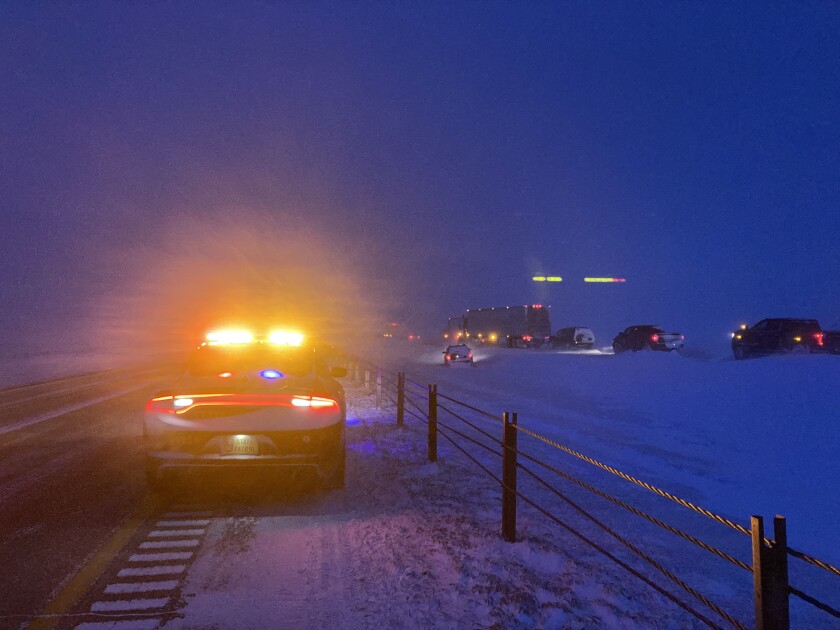 A deputy's emergency lights illuminate the left side of the photo. At right, several vehicles sit unmoving on a highway. At least one has entered the ditch.