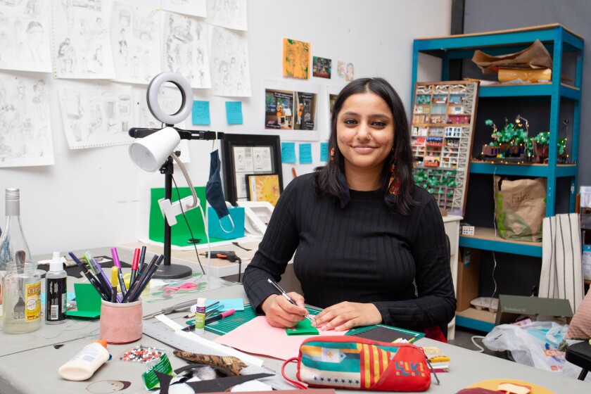 Roshan Ganu smiles as she works in her studio space with sketches lining the wall behind her