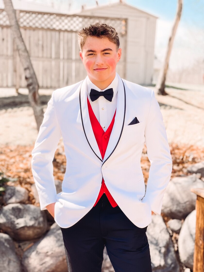 A boy in a white tux poses for a photo.