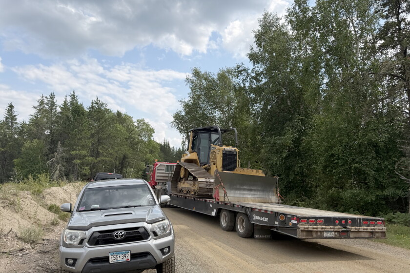 A bulldozer at rest on a large trailer parked on a gravel road.