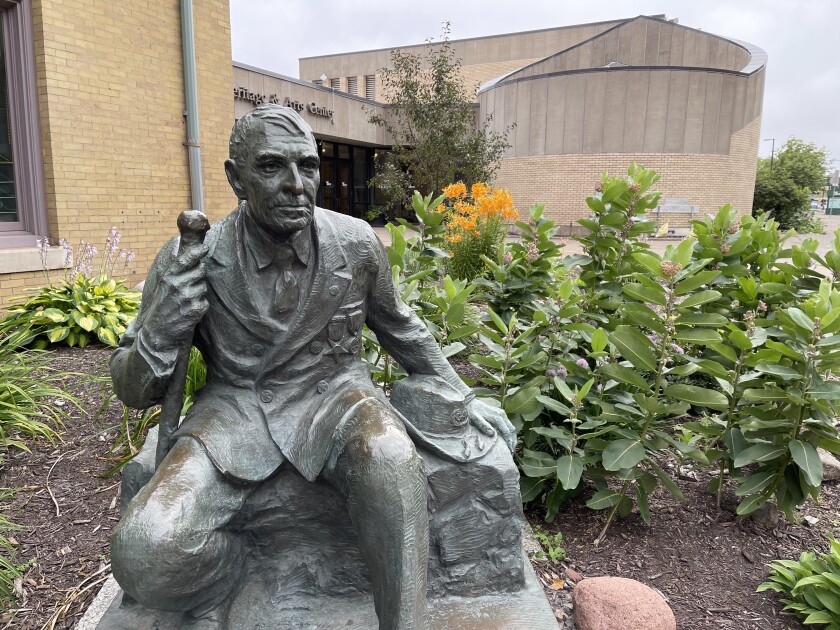 Statue of an elderly man seated on a low wall, with a wide-brimmed hat in the style of an American Civil War Union soldier seated next to him to his left.