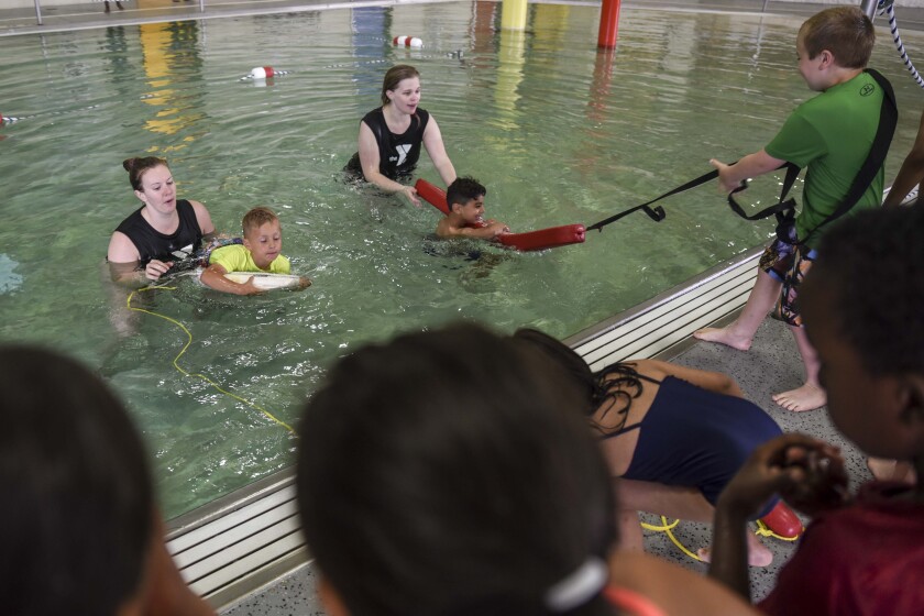 Erica Dischino / TribuneSwimming instructors Emily Nelson, left, and Taylor Flegel help kindergarten students practice how to save each other during the water safety portion of their summer school program Monday at the Kandiyohi County YMCA in Willmar.