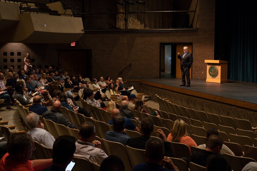 A suited man on a stage speaks to a crowd in an auditorium.