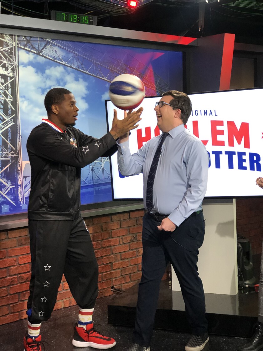 Flip White, in Harlem Globetrotters track suit, spins basketball on the finger of a man wearing a business suit.