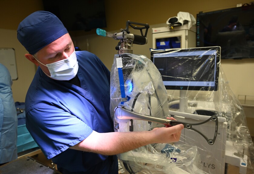 A doctor demonstrates a piece of robotic equipment that assists in knee replacements.