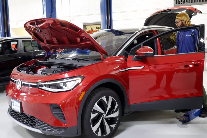A man stands in front of the open door of a shiny red small car.