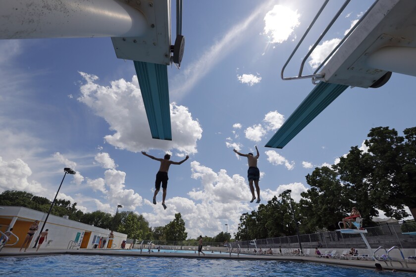 Two boys in mid-air jump off diving boards into a pool with a cloudy sky above.