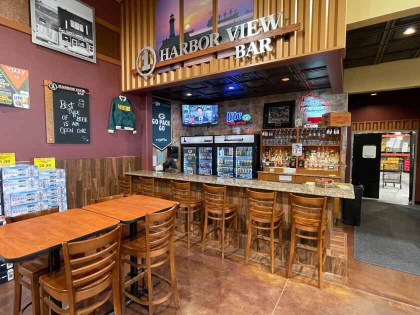 Barroom area with six seats along a bar and a two high-top tables nearer camera. Signage reads "Super One Harbor View Bar."