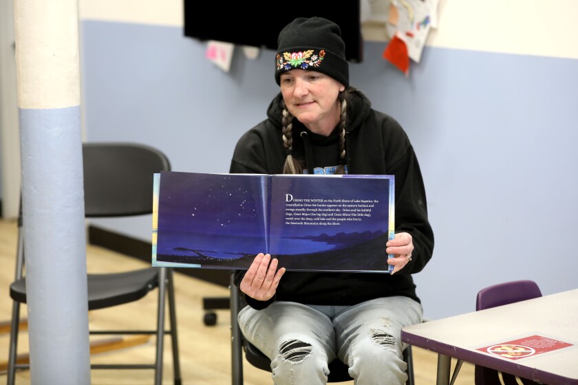 A woman holds up a children's book while reading it at and event.