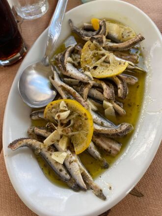 Small fish filets sit on a plate of olive oil with lemon wedges on top.