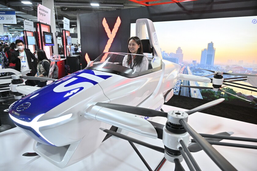 SkyDrive flying vehicle with a woman in the driver's seat sits on the showroom floor.