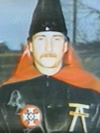 A mustached man wears the black and red robes of the "Aryan Nations" white supremacist group.