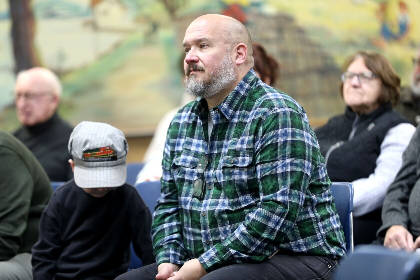 A man sitting in an audience listening to speeches at an indoor event.