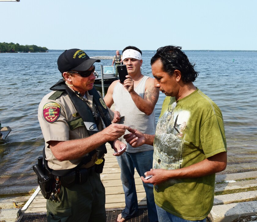 Area DNR officer Tim Collette issues a citation to Anishinabe Jim Northrup III while his boat partner Todd Thompson videotapes the event at the Hole-in-the-Day access to Gull Lake Friday morning. The two men were cited for illegally taking fish with a gill net. (Brainerd Dispatch/ Steve Kohls) Video