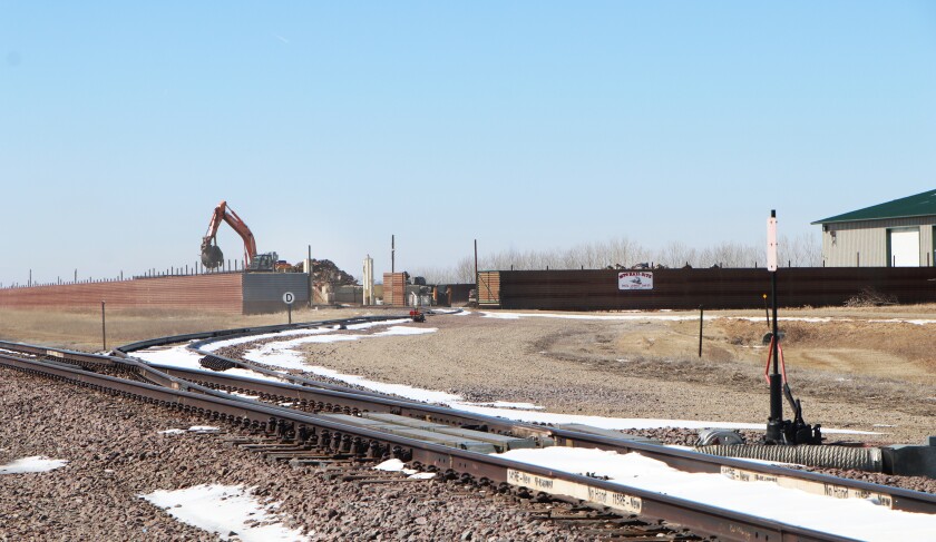The Meyers Tractor Salvage LLC rail spur leads to a car-loading facility, surrounded by a wall, where a backhoe places scrap iron into rail cars. At right is a machine shop that prepares recycled parts for shipping.
