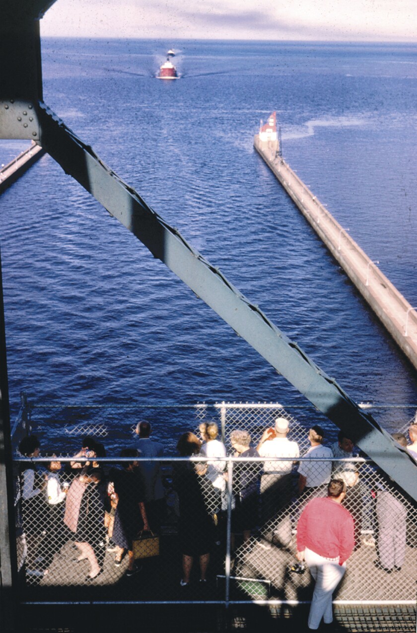 Photo of people standing in chain-link cage on the Aerial Lift Bridge, looking down at an incoming ship down the Duluth Ship Canal.