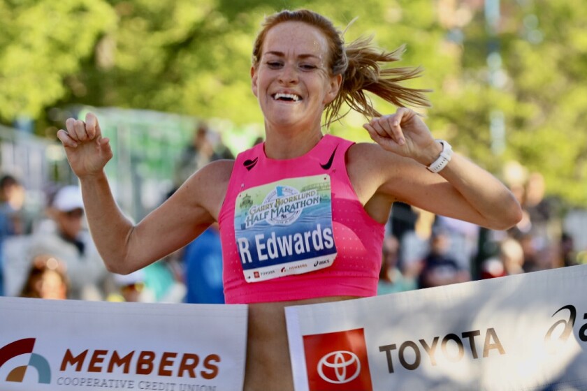 A female half-marathon runner, smiling, breaks through finish line tape