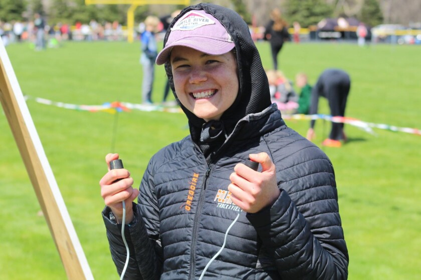 A woman in a black jacket holds timing devices at a track meet.