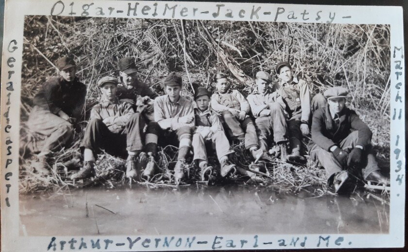 A group of boys wear skates and sit by the edge of ice in this black and white photo.
