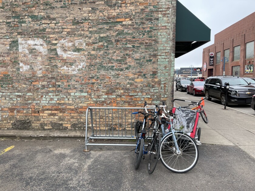 Bicycles crowd a rack positioned against a brick wall with faded paint.
