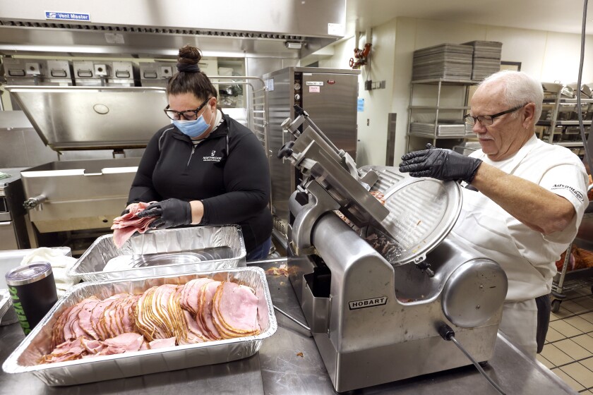 Woman stacks sliced ham while man slices ham.