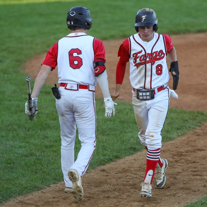 Fargo Post 2's Sam Ovsak gives Caleb Briggeman five after he scores a run on a bases-loaded walk against Thief River Falls Post 117 on Friday, June 27, 2025, at Jack Williams Stadium in north Fargo.