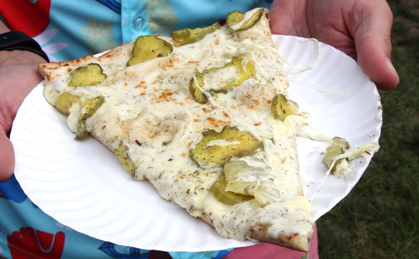 Pizza covered in pickles served on a paper plate.