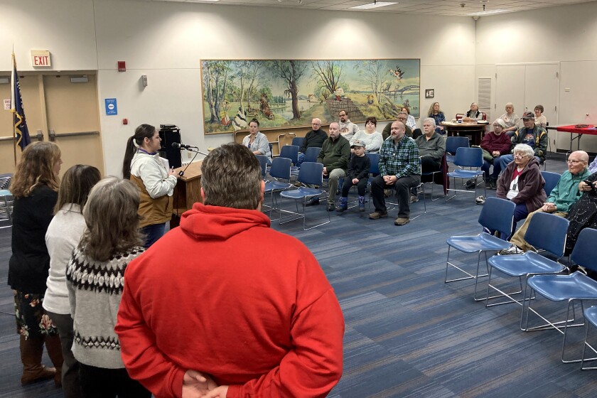 People standing near a podium while other people sit in chairs during an indoor event.