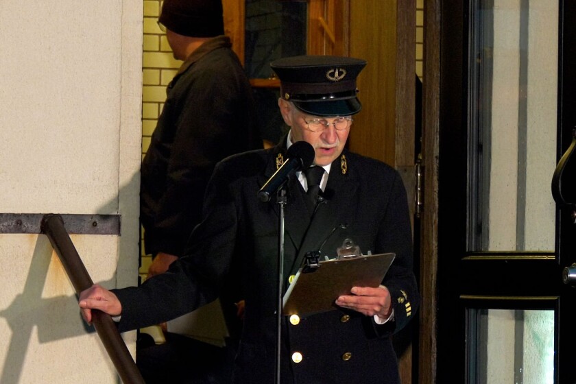 A man reading names from a clipboard into a microphone during a ceremony.