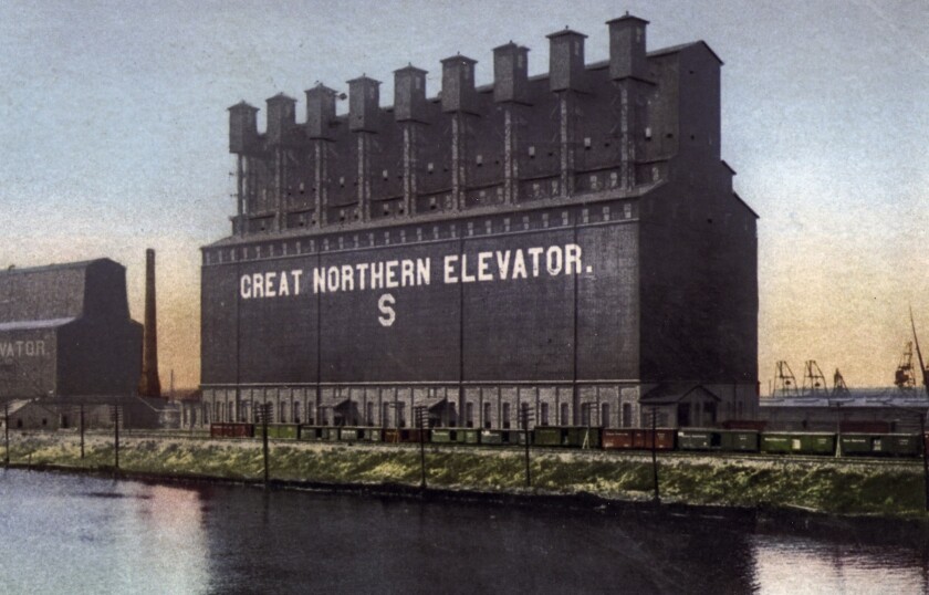 A colorized vintage postcard photo of a large lakeside grain elevator with the words GREAT NORTHERN ELEVATOR written on the side.