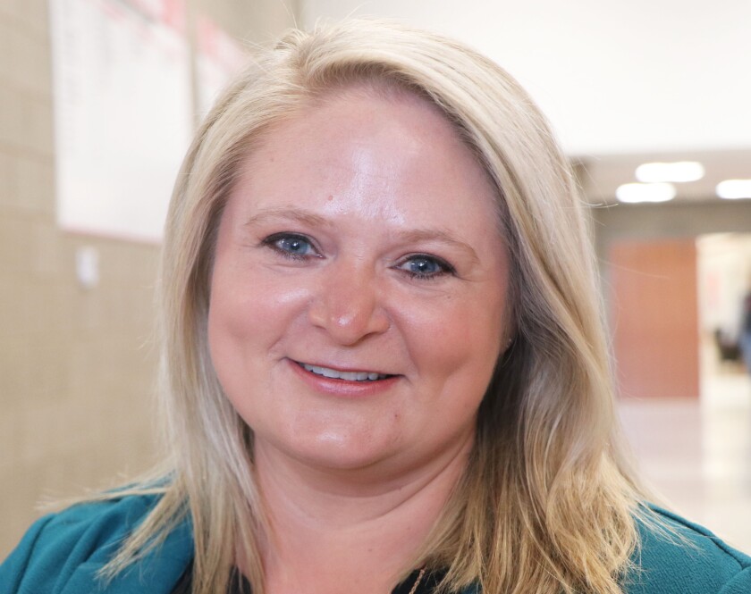 A light-haired smiling woman poses for a face photo in a high school hallway.