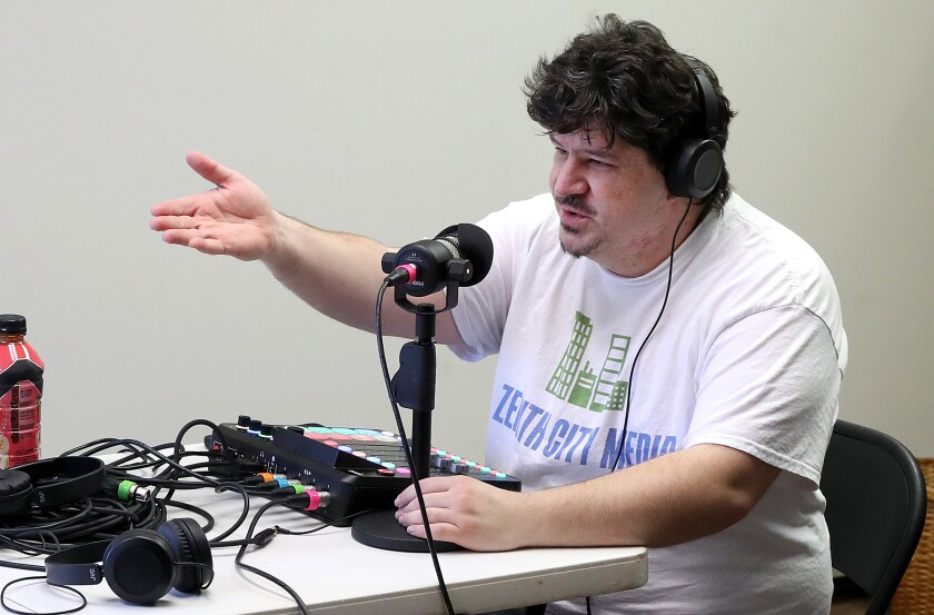 Man sits behind microphone and motions with hand as he talks.