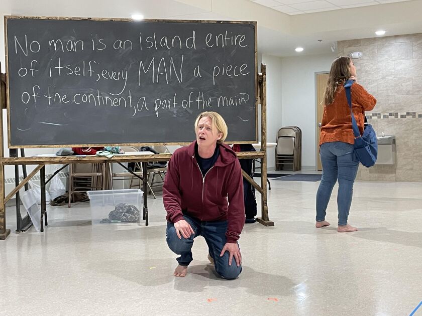 One person takes a knee while another person stands with their back to them. Behind is a blackboard