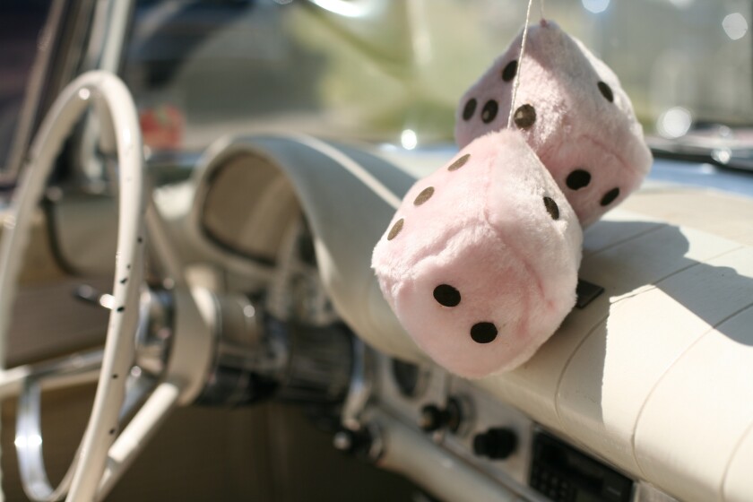 pair of large white fuzzy dice hang from rearview mirror in vintage car with white interior