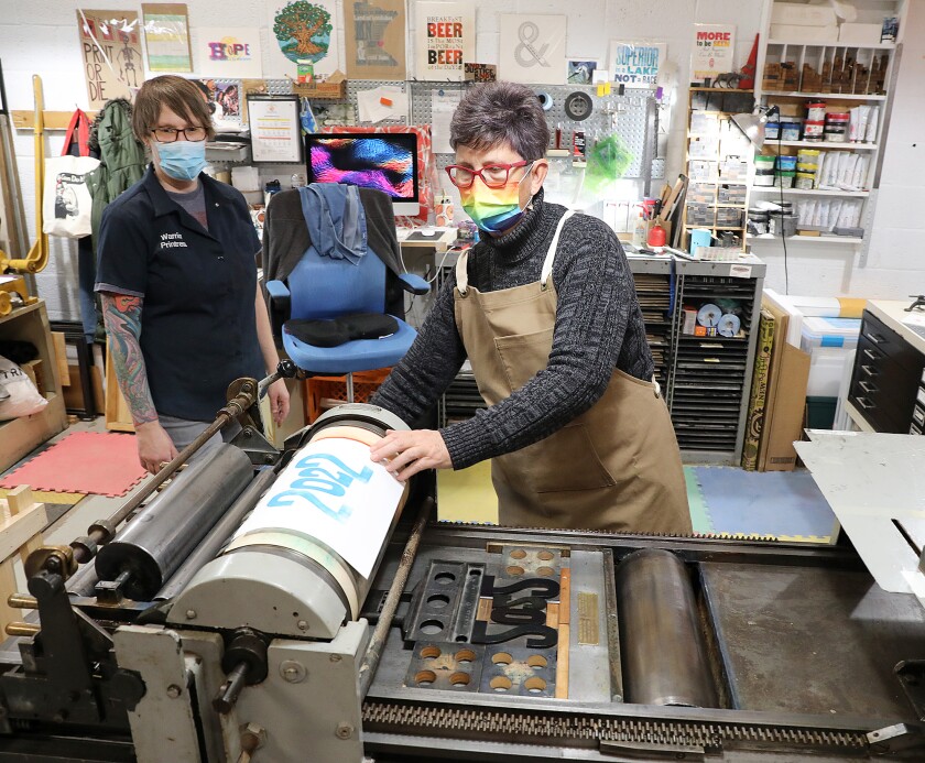 Stacie Renne checks a test run of a print at Warrior Printress as Janelle Miller watches
