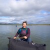 light-skinned woman wearing personal flotation device smiles as she holds paddle in canoe