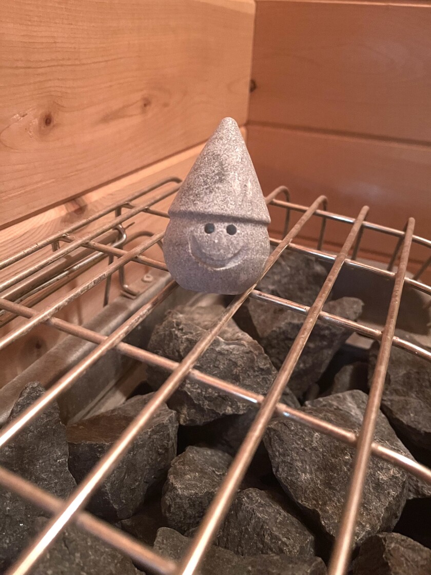 Stone in shape of smiling round face with pointy hat, seen on a metal grille over rougher stones.