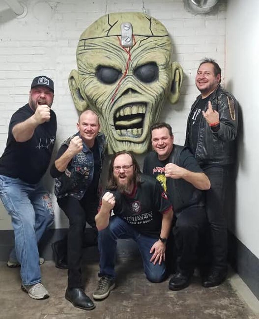 Five white men pose with large horrific zombie face, holding their fists aloft.