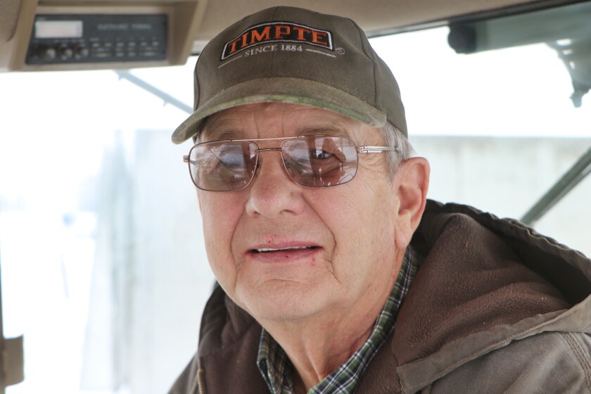 A farmer in a cap in his tractor cab, stops for a photo.