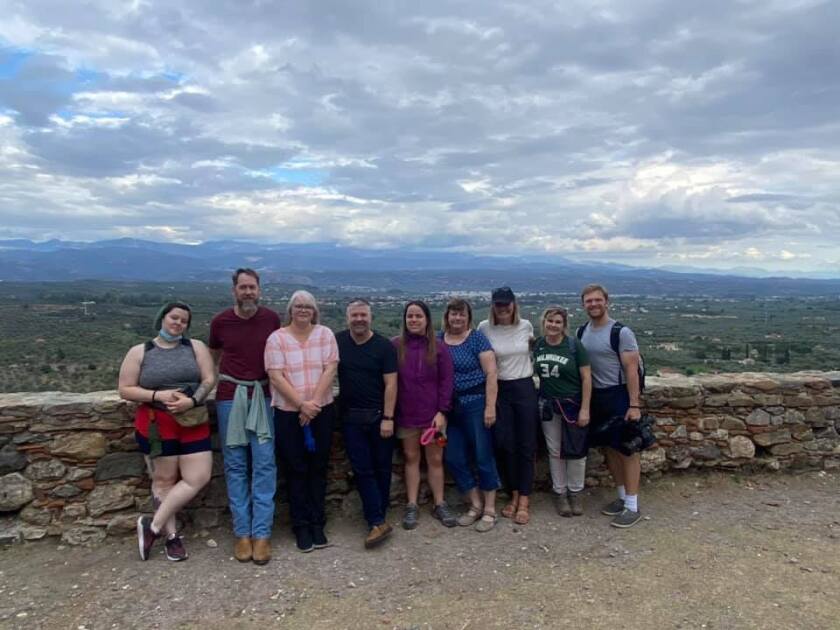 Nine people line up in front of an old stone wall for a photo.